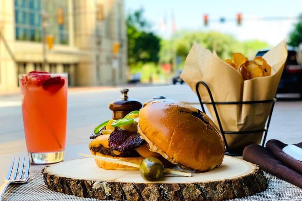 Gourmet burger with fries and cocktail served outdoors with city views