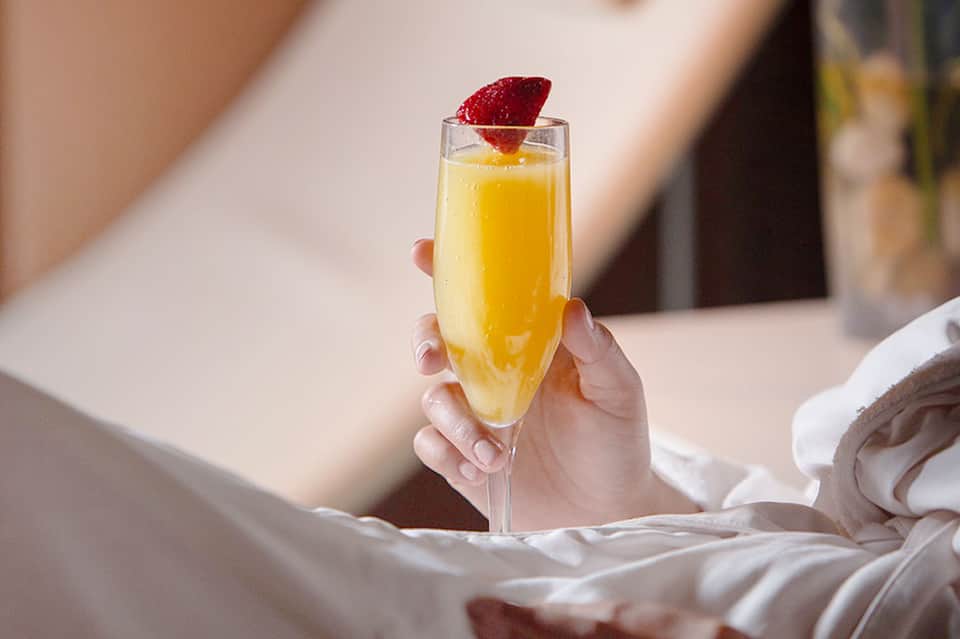 Hand holding mimosa cocktail with strawberry garnish in bright sunlight