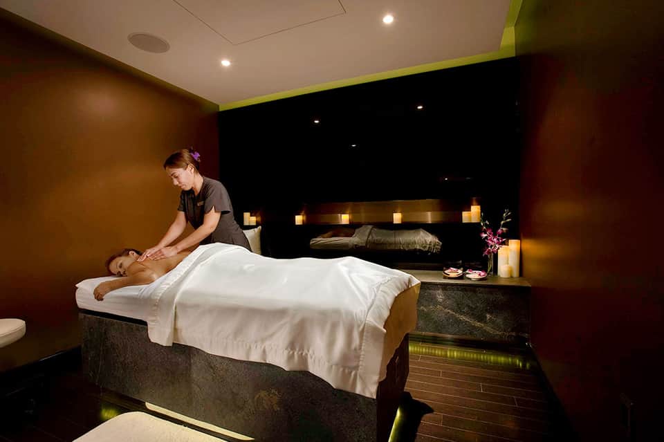 Spa therapist performing massage on client in dimly lit treatment room with candles