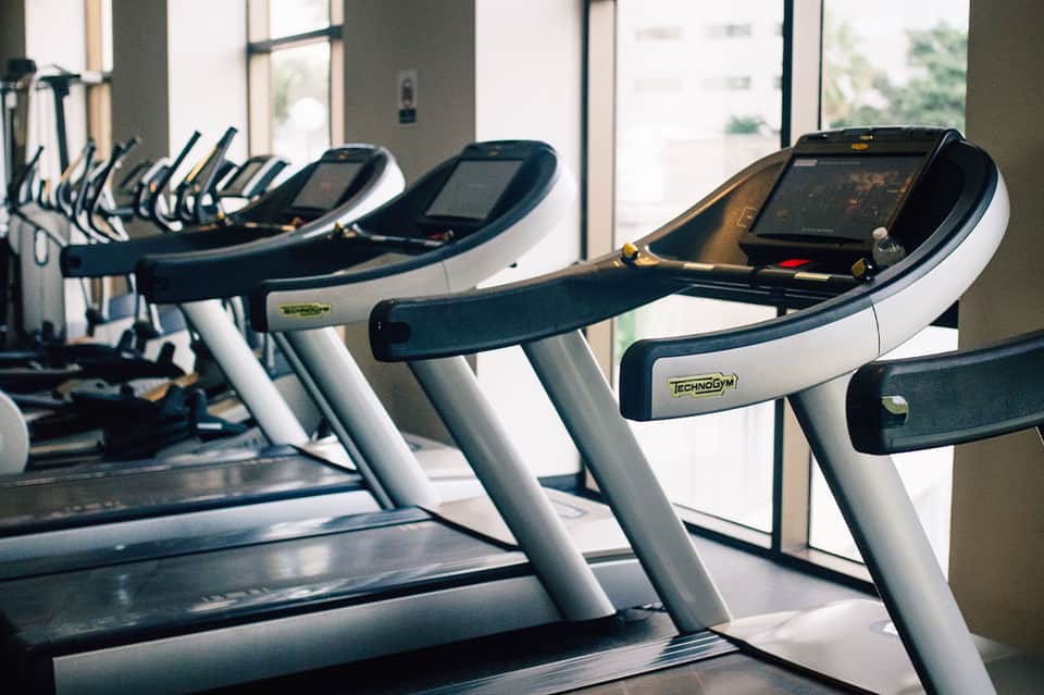 Modern gym with treadmills and exercise equipment lined up beside floor-to-ceiling windows