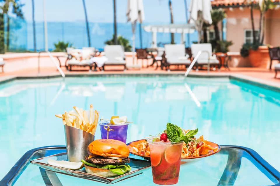 Pool deck dining with burger, fries, cocktail, and appetizer plate overlooking resort swimming pool
