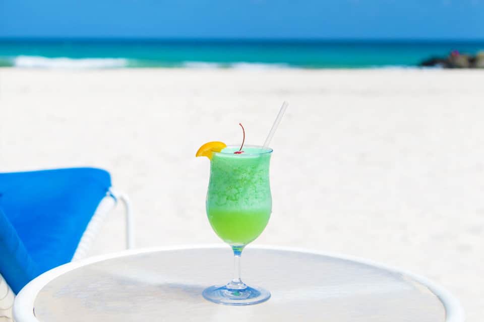 Green tropical cocktail with cherry and lemon slice on beach table