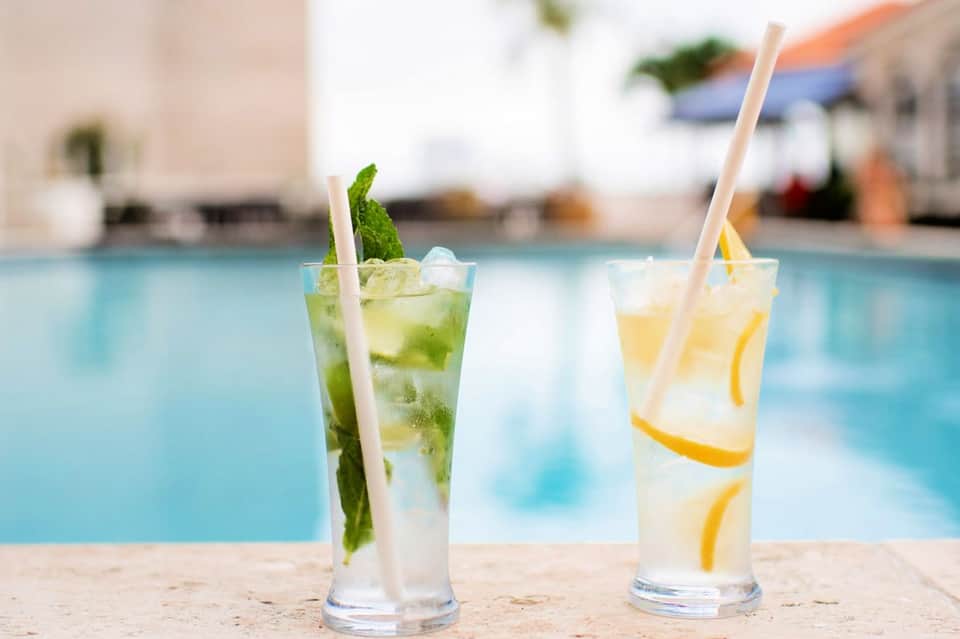 Two refreshing cocktails with straws by a swimming pool, one with mint garnish and one with lemon slices