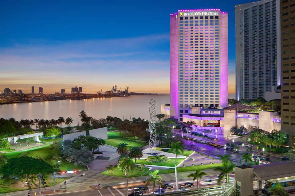Inter-Continental hotel illuminated in purple at dusk with riverside city skyline and palm trees visible in background
