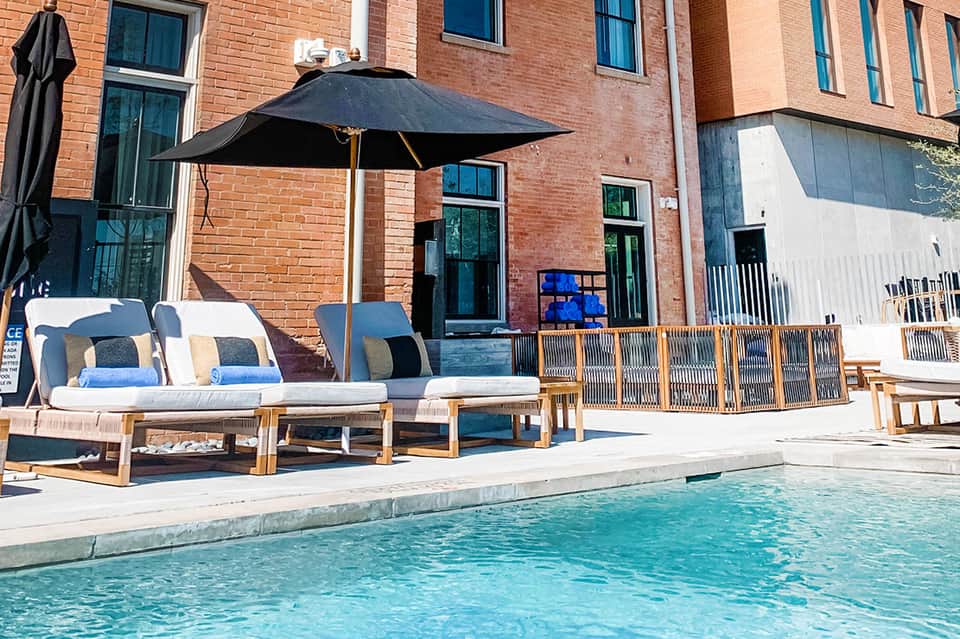 Modern pool deck with black umbrella, wooden lounge chairs, and brick building