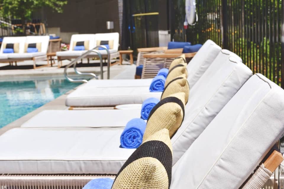 Poolside lounge chairs with white cushions, blue rolled towels, and straw hats arranged in a row by the pool