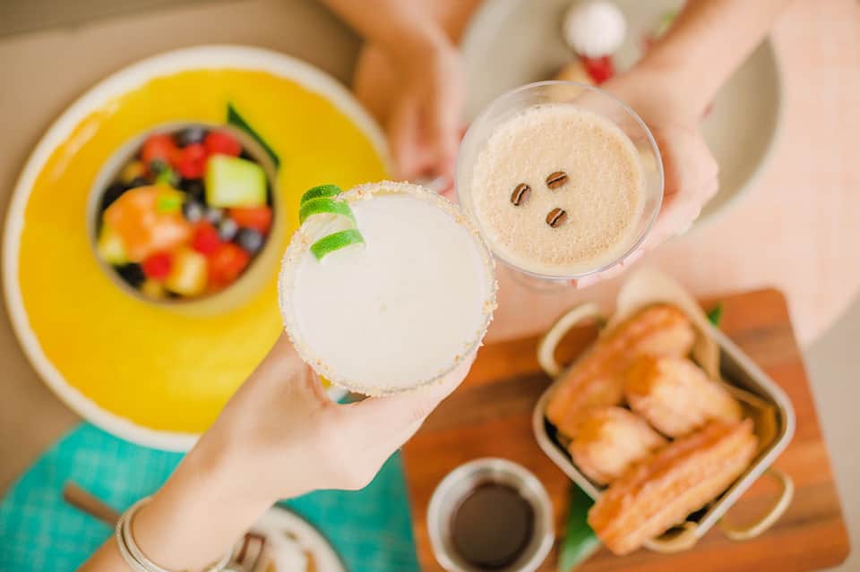Two cocktails with salt-rimmed glasses and mint garnish; colorful fruit salad visible