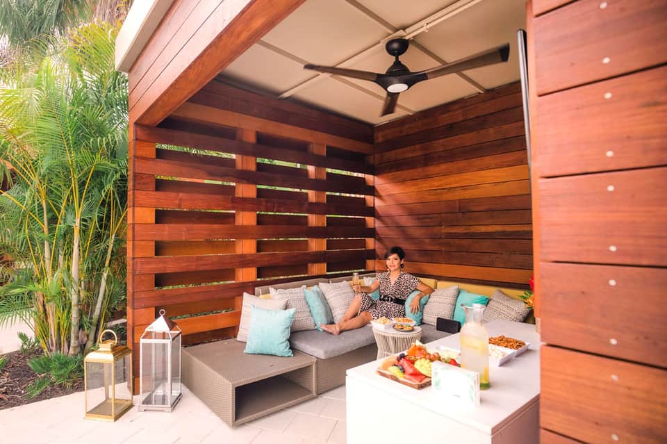 Modern wooden pergola lounge area with cushioned seating, pillows, and refreshments outdoors