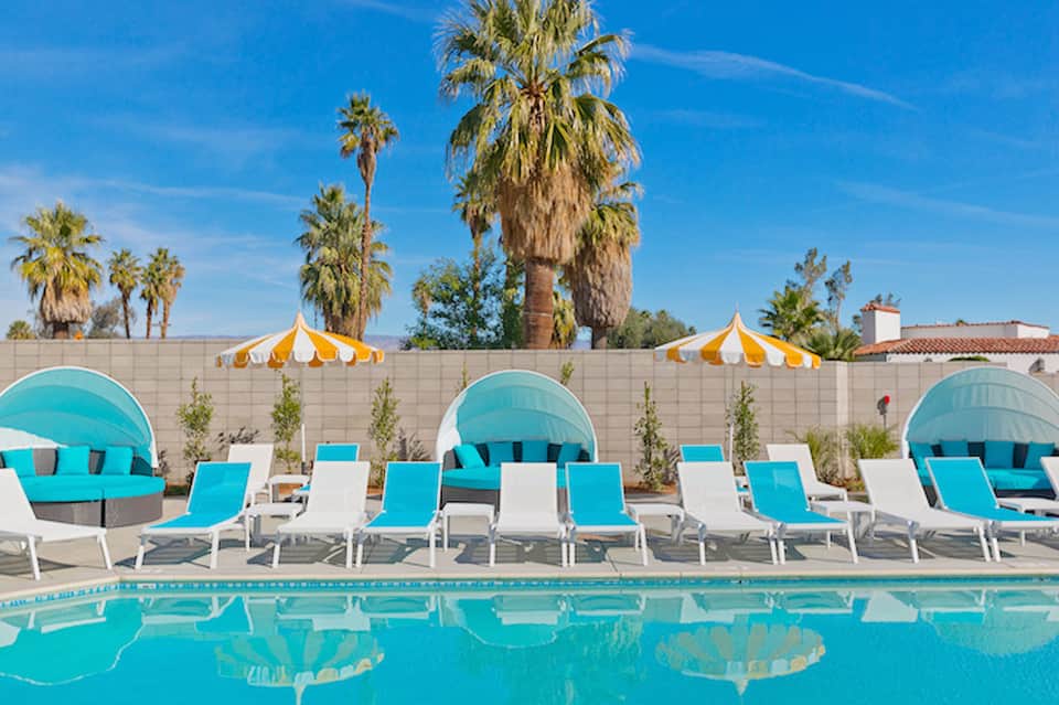 Pool deck with turquoise loungers, yellow umbrellas, and palm trees