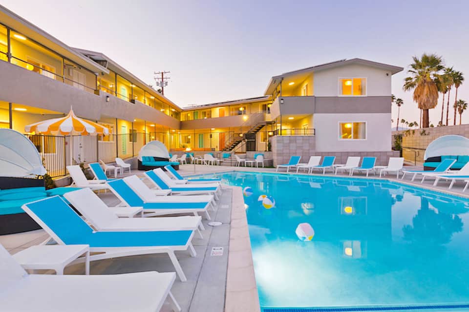 Resort pool area at dusk with blue loungers, illuminated buildings, and palm trees