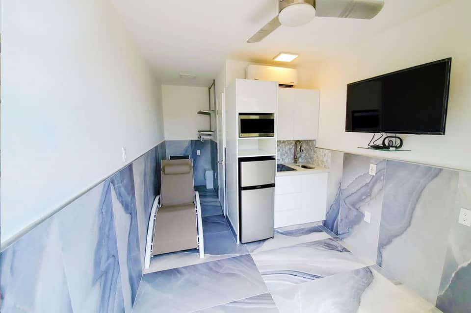 Narrow RV or mobile home interior with kitchen, appliances, seating, and blue marble-effect flooring