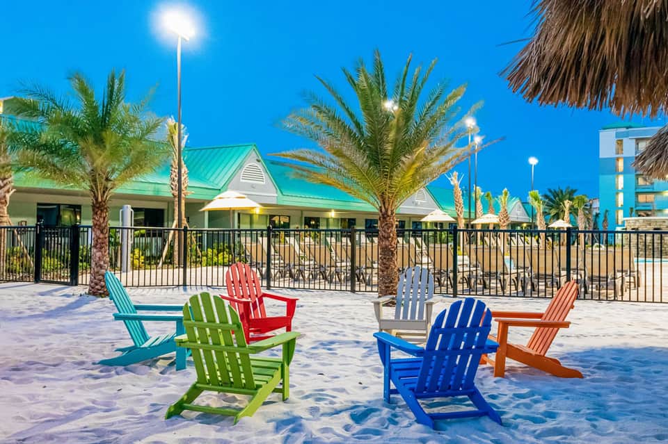 Colorful Adirondack chairs on sandy beach with palm trees and resort buildings