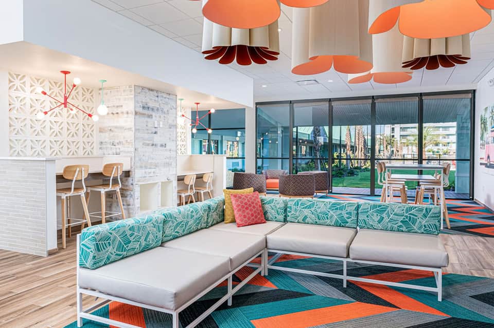 Modern resort lounge with teal patterned seating, orange pendant lights, and floor-to-ceiling windows