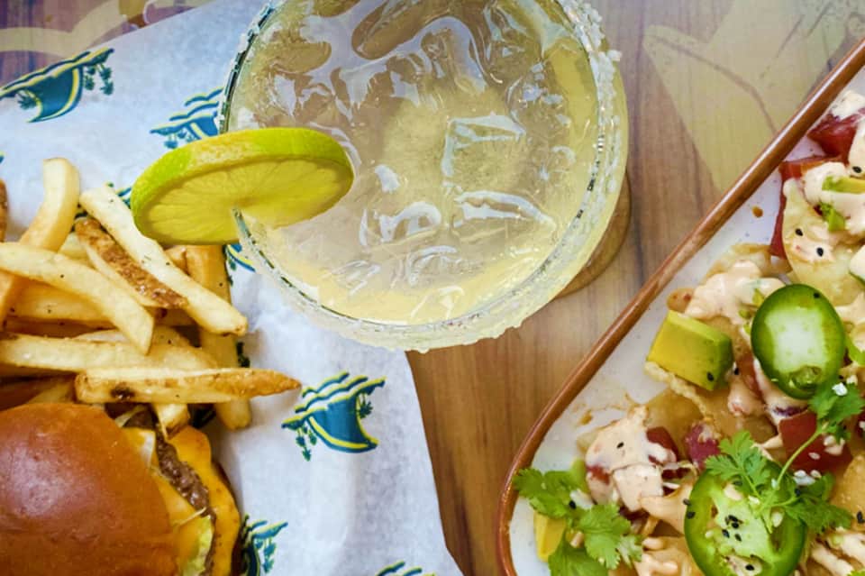 Margarita with lime slice, burger and fries, and ceviche dish at beachfront restaurant