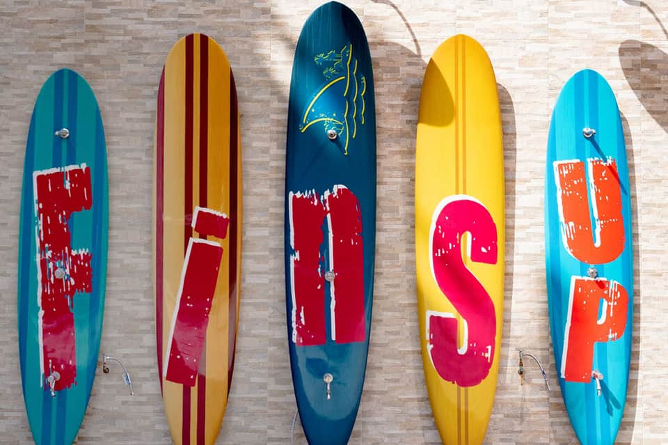 Five colorful surfboards displayed on brick wall with red and yellow graphics and designs