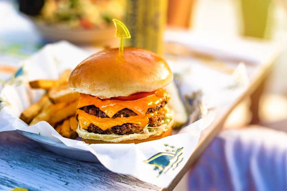 Double cheeseburger with golden bun and fries on white paper wrapper by pool