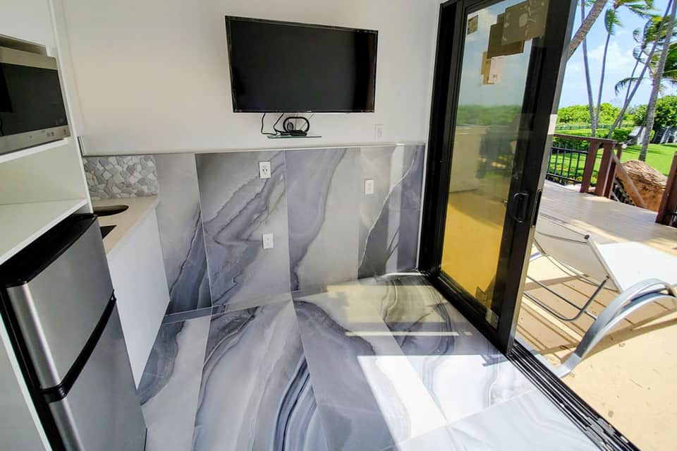 Modern kitchenette with marble backsplash, flat-screen TV, and sliding glass doors opening to ocean view