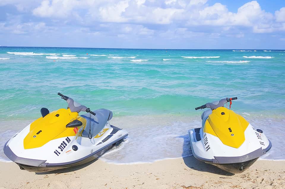 Two yellow and white jet skis lined up on sandy beach with turquoise ocean and waves