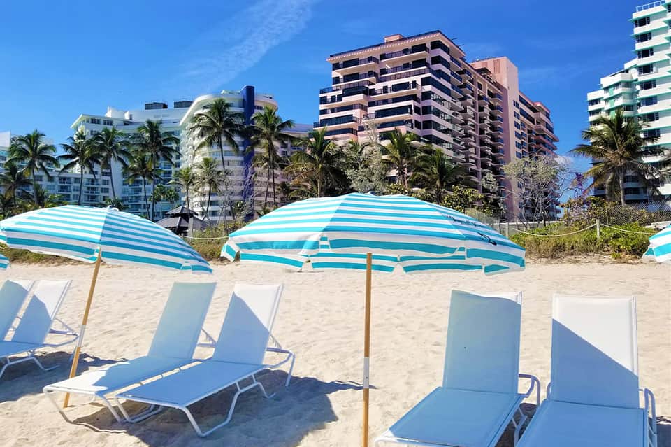 Beach scene with striped umbrellas, lounge chairs, and residential buildings