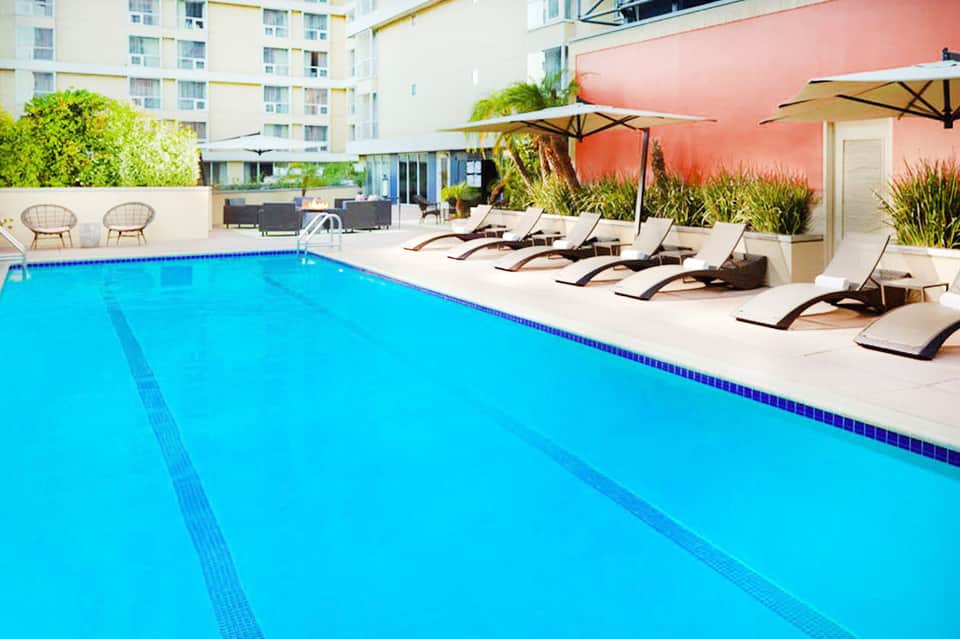 Resort swimming pool with lane markings, lounge chairs, umbrellas, and modern apartment buildings in background