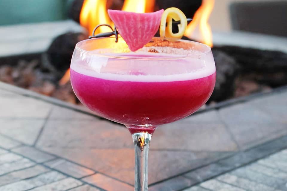 Pink cocktail with fruit garnish served by fire pit at dusk
