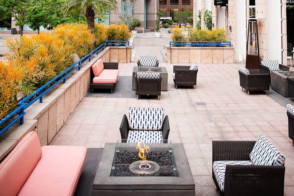 Rooftop patio with fire pit, black wicker chairs, pink seating, and yellow ornamental grasses