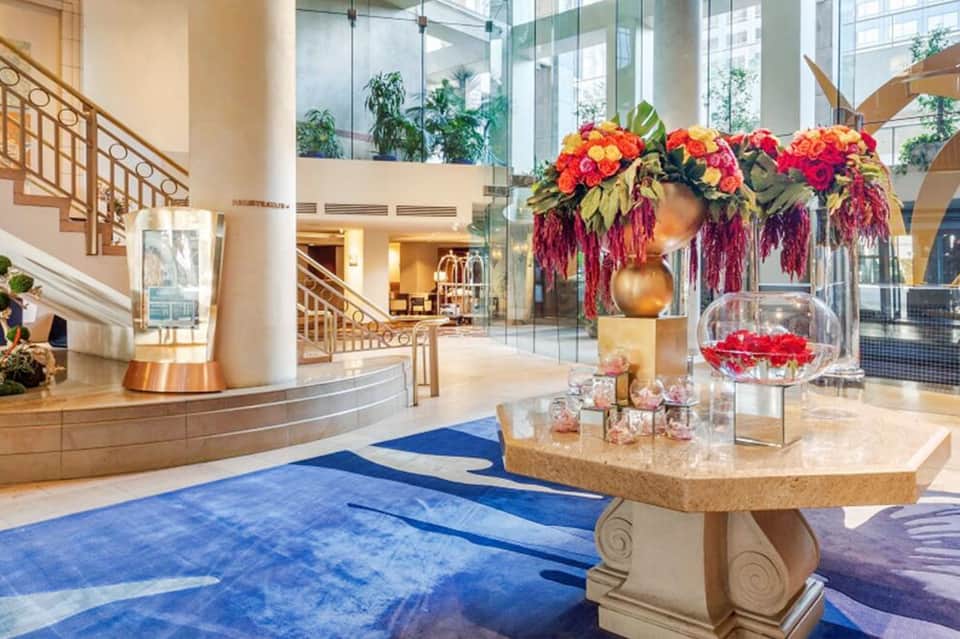 Luxury hotel lobby with marble floors, floral arrangement, and grand staircase