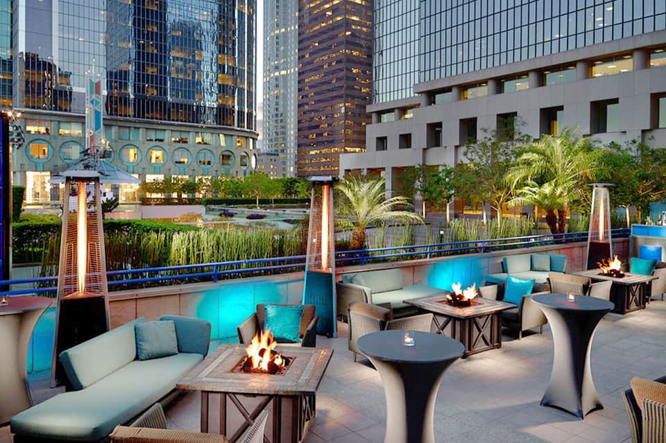 Rooftop lounge with fire pits, modern seating, and illuminated pool overlooking downtown city skyline