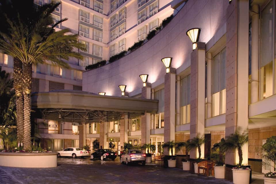 Elegant hotel porte-cochere entrance at dusk with palm trees and luxury vehicles