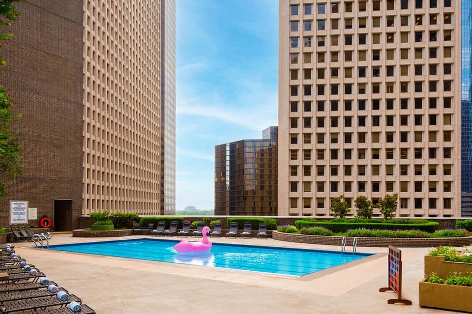 Outdoor pool with pink float surrounded by lounge chairs between tall residential buildings