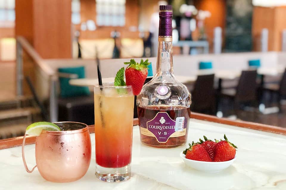 Cocktails and Courvoisier cognac bottle with fresh strawberries on white table at resort bar