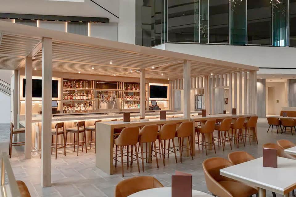 Modern hotel bar lounge with wooden pergola, tan leather seating, and illuminated bar counter