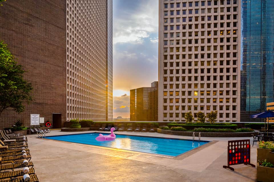 Urban rooftop pool surrounded by high-rise buildings at golden hour with pink flamingo float