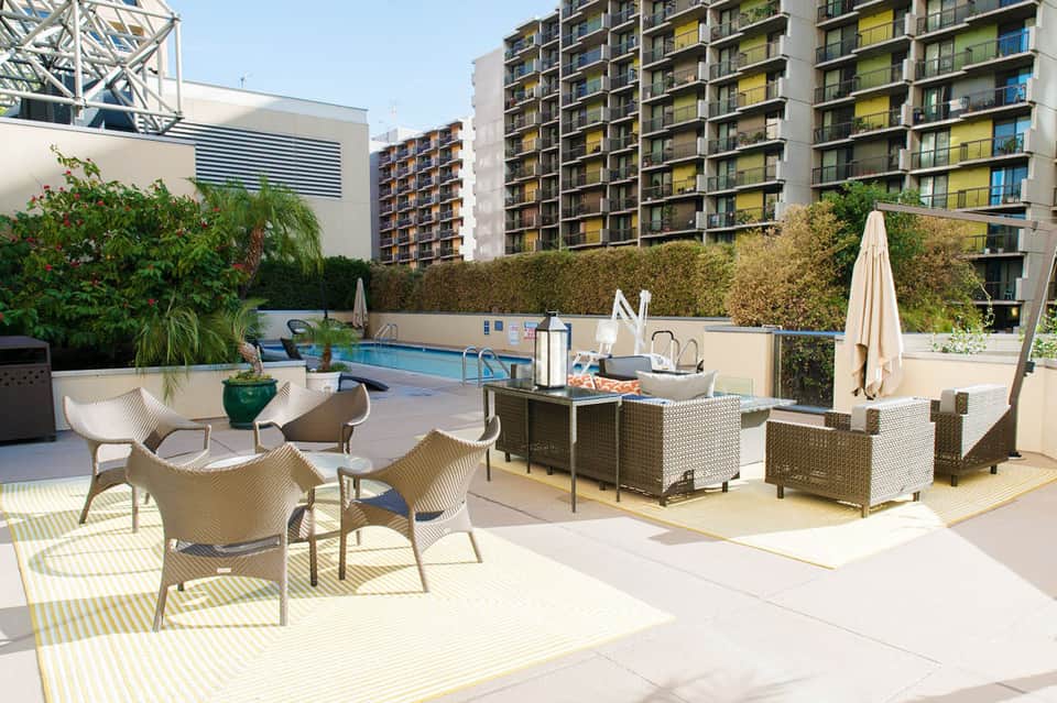 Rooftop pool deck with lounge chairs, umbrellas, and casual seating area surrounded by residential buildings