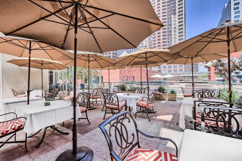 Outdoor terrace with white umbrellas, dining tables, and high-rise buildings in urban setting