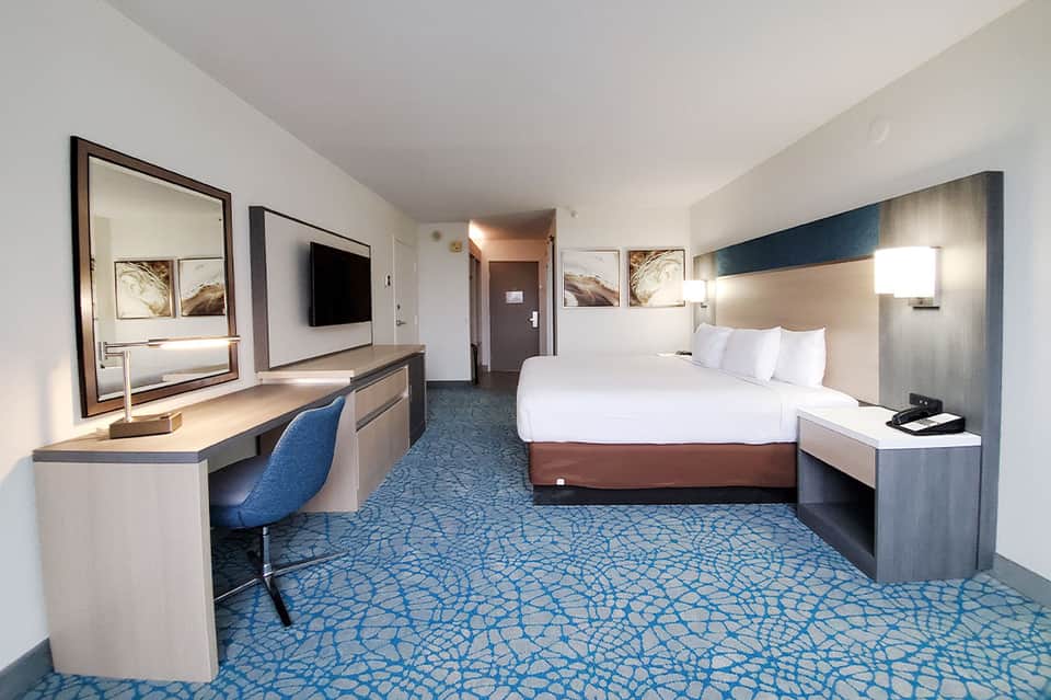 Modern hotel room with queen bed, work desk, flat-screen TV, and blue patterned carpet