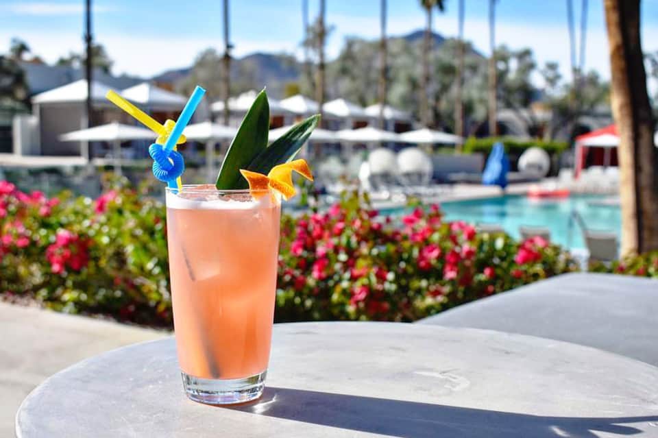 Tropical cocktail with colorful straws by pool at resort with palm trees and lounging area