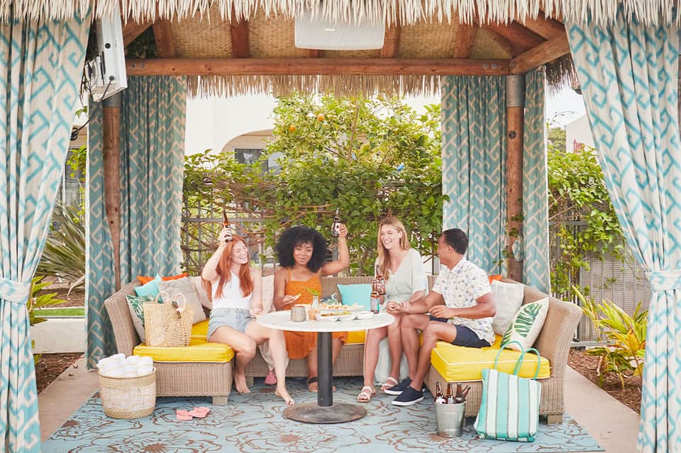 Four guests socializing on cushioned seating under a teal patterned cabana with tropical decor