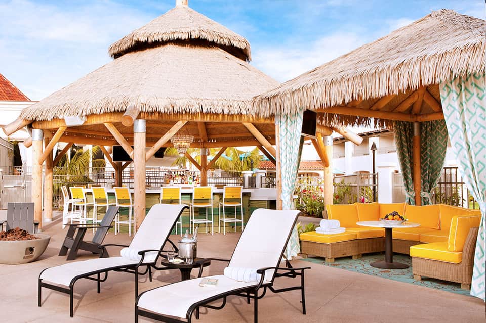 Beachfront resort patio with thatched-roof cabanas, yellow lounge chairs, and ocean views