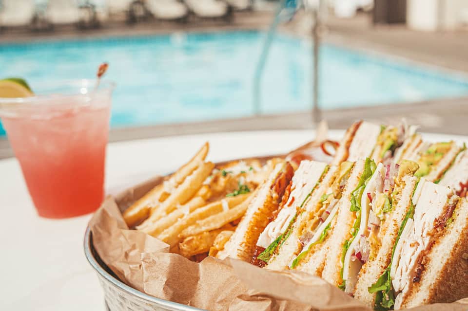 Poolside lunch spread with sandwiches, fries, and pink beverage