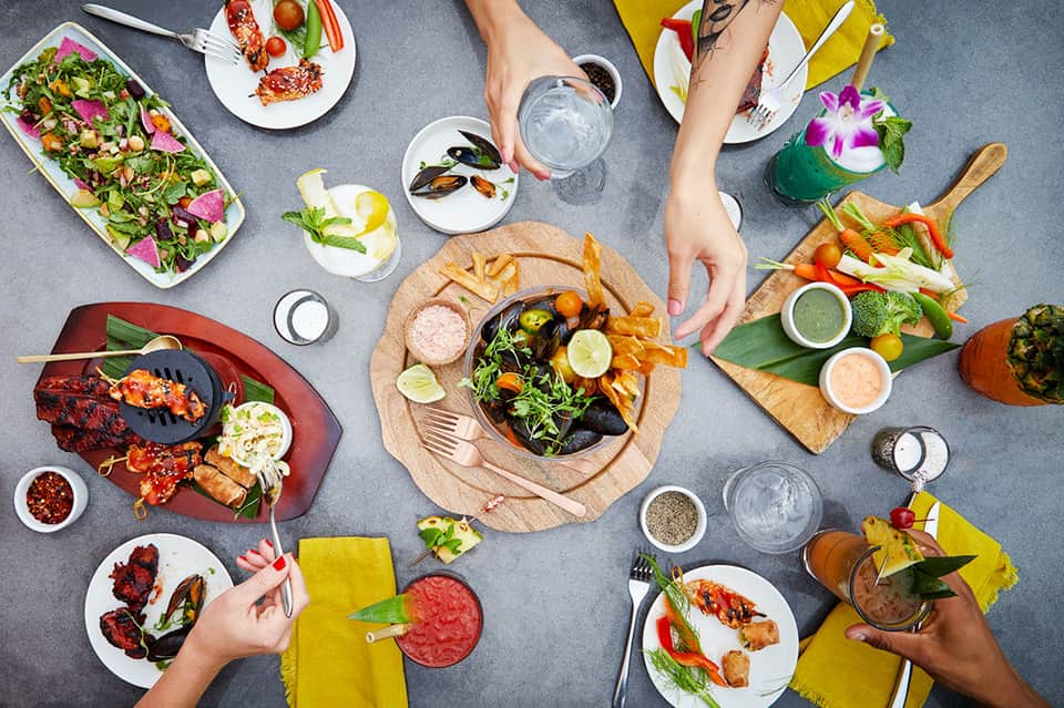 Overhead view of upscale dining with seafood, salads, and cocktails shared among multiple diners