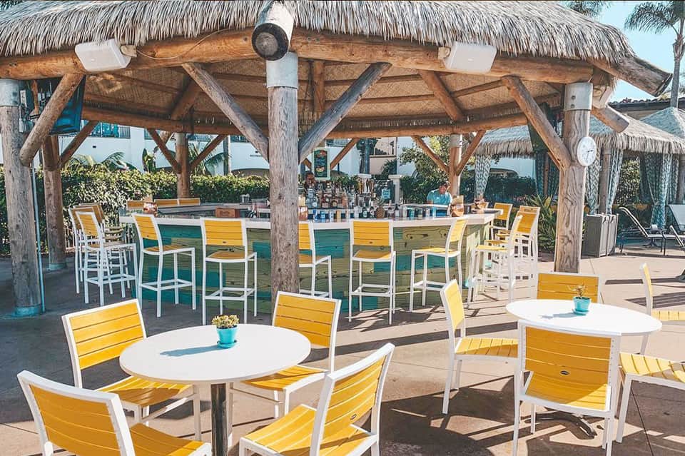 Beachfront tiki bar with yellow seating, wooden pergola, and blue ocean views in tropical setting