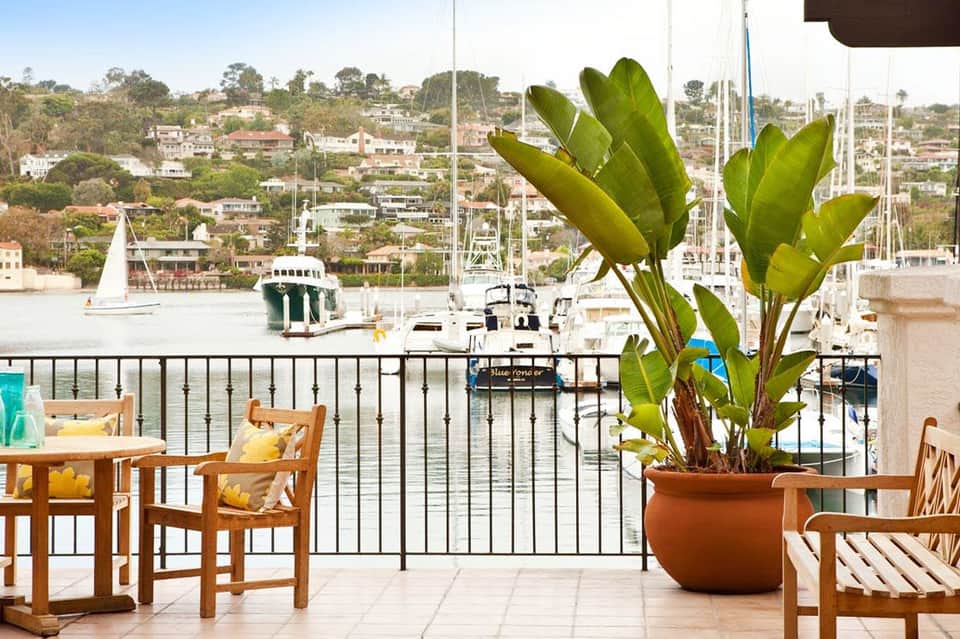 Marina waterfront terrace with wooden chairs, potted plant, and sailboats in background