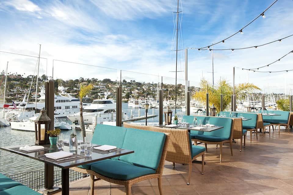Waterfront dining area with turquoise chairs, sailboats, and marina views
