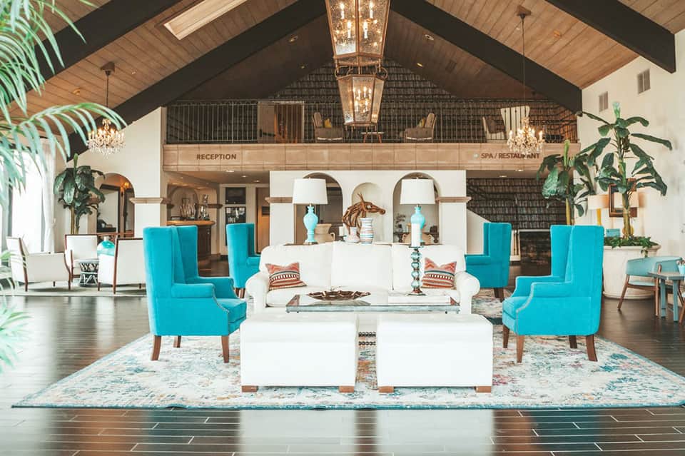 Elegant hotel lobby with vaulted ceiling, turquoise accent chairs, white sofas, and two-story mezzanine design