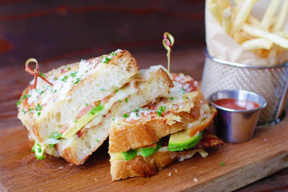 Gourmet sandwich with ham, cheese, and greens on toasted bread with fries and sauce