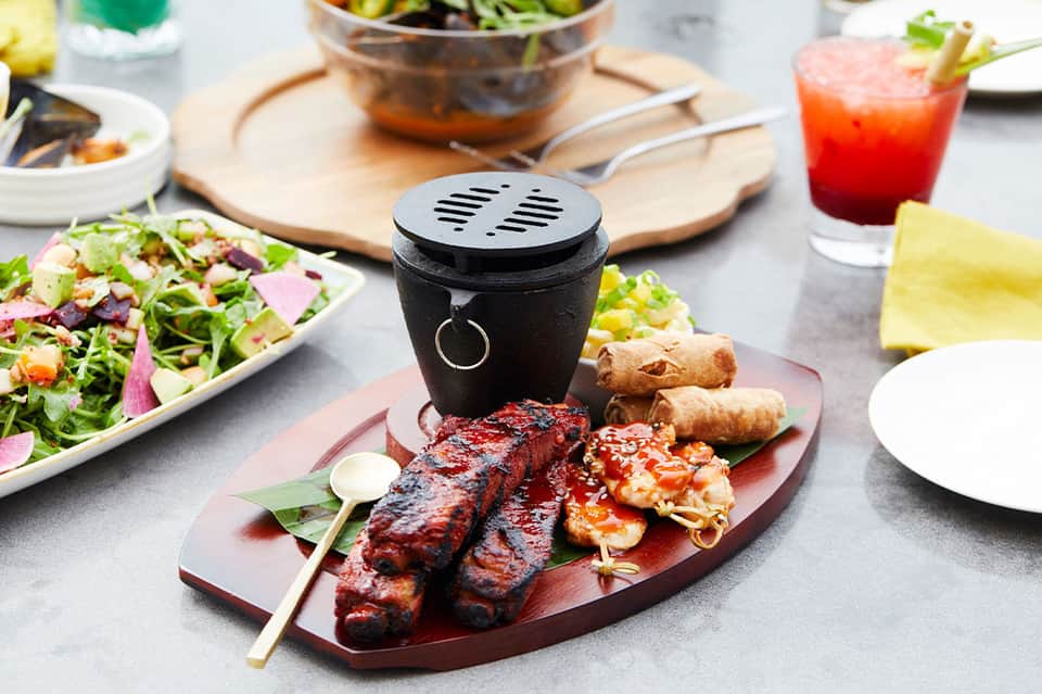 Fine dining table with grilled meats, fresh salads, and decorative black pot