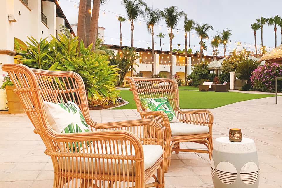 Rattan lounge chairs with white cushions on a patio overlooking manicured lawn and palm trees