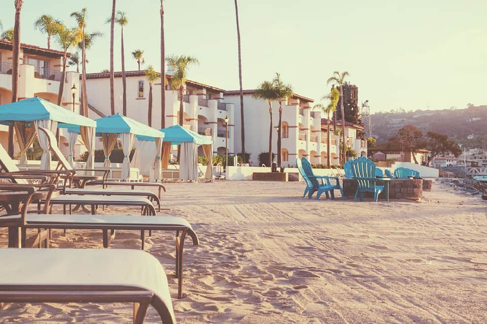 Beach resort with turquoise umbrellas, lounge chairs on sand, and Spanish colonial-style buildings