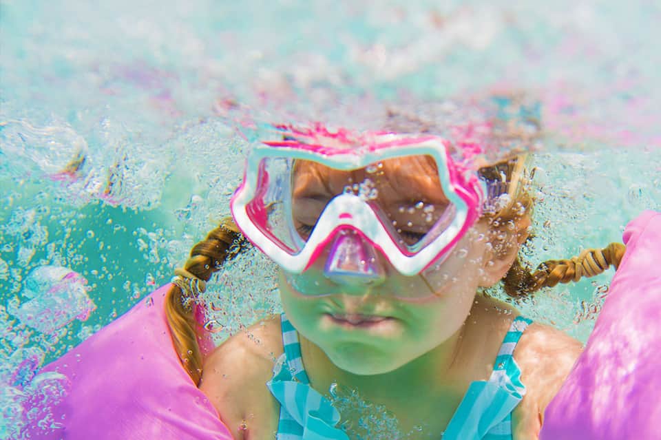 Child wearing colorful snorkel gear underwater in a swimming pool with vibrant water effects